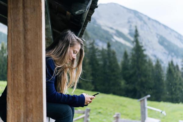 Imagen de una chica en las montañas usando u móvil apoyada en una barandilla