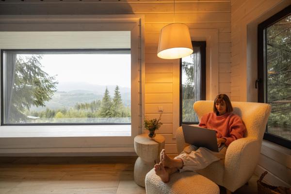 Mujer trabajando en su casa y ventana grande detrás con paisaje